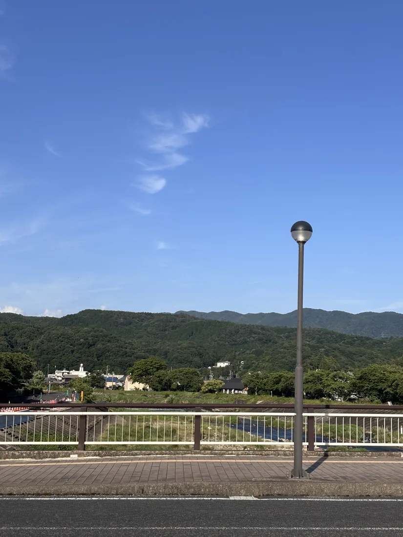 岐阜県瑞浪市の風景。青空と山並み、川沿いの道と街灯